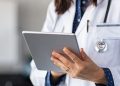 Close up of woman doctor hands using digital tablet at clinic. Closeup of female doctor in labcoat and stethoscope holding digital tablet, reading patient report.