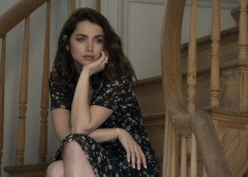A woman sits on a staircase with her hand under her chin.