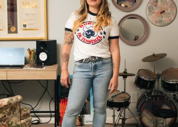 A woman wearing a "Bury Me in Tennessee" shirt stands in front of a set of drums.
