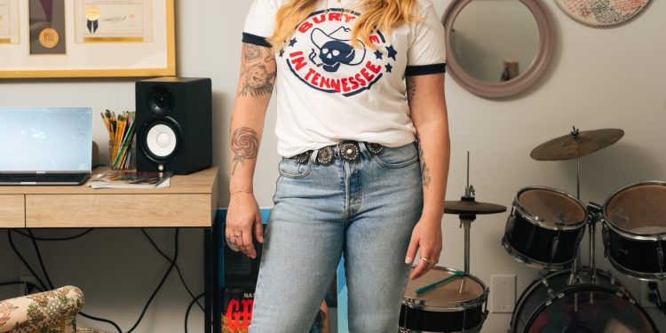 A woman wearing a "Bury Me in Tennessee" shirt stands in front of a set of drums.