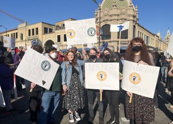Starbucks workers stand in the street holding signs that read, “Union yes,” “Union busting is disgusting,” and “Coffee’s the game, union strong’s the name.”