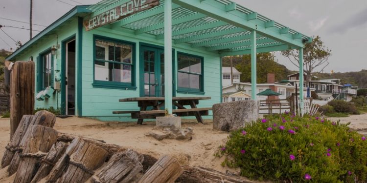 A green beach cottage with a sign that reads "Crystal Cove."