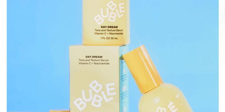Three yellow Bubble Skincare Day Dream Vitamin C + Niacinamide Tone And Texture Serum bottles and packaging on blue background