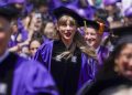 A blond woman wearing a velvet black graduation cap and purple graduation gown in a crowd