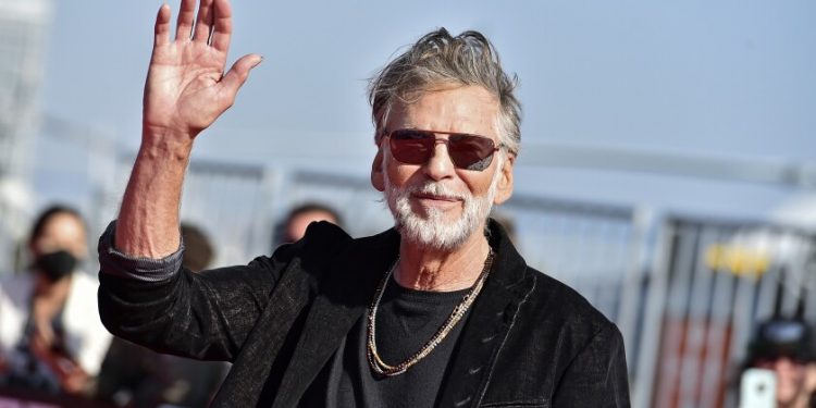 A man with gray hair and a beard waves as he walks.