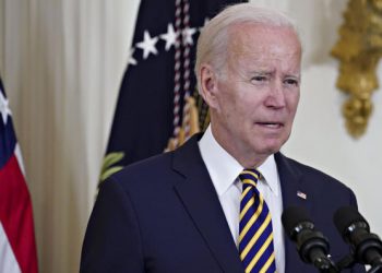 Joe Biden speaking into a microphone with an American flag behind him.