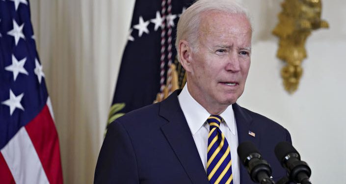 Joe Biden speaking into a microphone with an American flag behind him.