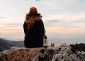 A woman sits on a mountain ledge with a bottle of High West Distillery's Campfire whiskey.