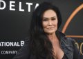 A woman with long dark hair in a black jacket on a red carpet