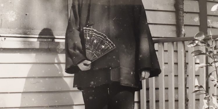 An old black-and-white photo of a man standing on a porch, a small dog at his feet.